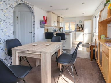 A kitchen and dining area with a wooden table, black chairs, white cabinets, and a white refrigerator at Sunny South Shore in Bridlington