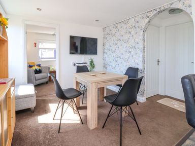 A dining area with a wooden table and four black chairs a wall-mounted television and an archway in the background at Sunny South Shore in Bridlington