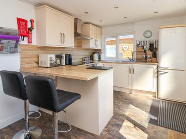 A kitchen with two black bar stools a microwave and refrigerator at Sunny South Shore in Bridlington