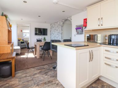 An open kitchen and dining area with white cabinets black chairs a wooden table and a wall mounted tv at Sunny South Shore in Bridlington