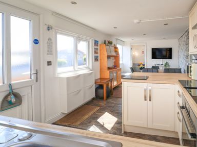 A kitchen with white cabinets and wooden countertops next to a dining area with chairs and a wall-mounted TV at Sunny South Shore in Bridlington