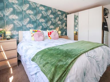 A bedroom with a double bed green throw pillows bedside tables and a white wardrobe at Sunny South Shore in Bridlington