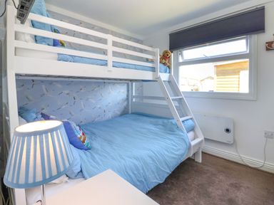 A bedroom with a white bunk bed blue bedding a bedside lamp and a window with a dark blind at Sunny South Shore in Bridlington