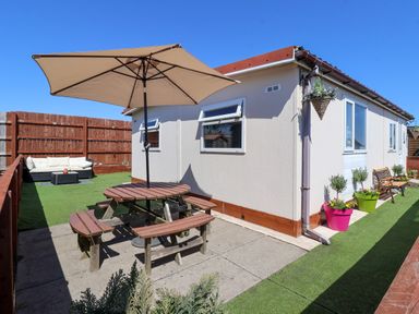 An outdoor patio area with a picnic table and umbrella next to a single-story building at Sunny South Shore in Bridlington