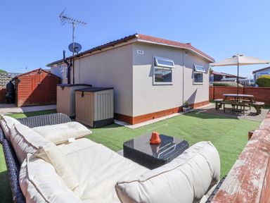 An outdoor patio area with a cushioned sofa a small table a shed and a picnic table with an umbrella at Sunny South Shore in Bridlington