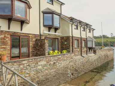Exterior view of a two story stone and stucco house with bay windows overlooking a waterway at 7 Island Quay in Salcombe