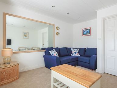 A living room with a blue sofa a wooden coffee table a large wall mirror and a lamp on a wooden side table at 7 Island Quay in Salcombe