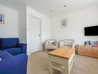 A living room with a wooden coffee table a blue sofa two armchairs a wall-mounted television and a wooden cabinet with books at 7 Island Quay in Salcombe
