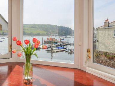 A vase with red tulips on a wooden windowsill with a view of boats and green hills at 7 Island Quay in Salcombe