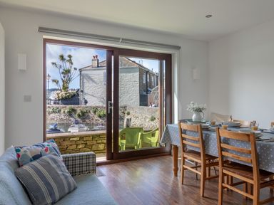 A dining area with a wooden table and chairs and a sofa near sliding glass doors overlooking boats and buildings at 7 Island Quay in Salcombe