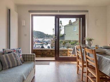 A dining area with a wooden table and chairs and a sofa next to a large window showing boats on water at 7 Island Quay in Salcombe