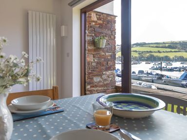 A dining table with plates glass of orange juice and flowers near a large window overlooking boats on the water at 7 Island Quay in Salcombe