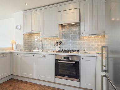 A kitchen with white cabinets a built in oven a gas stove a sink and a kettle at 7 Island Quay in Salcombe