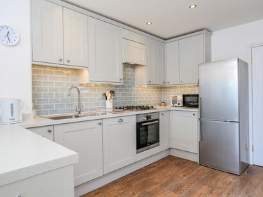 A kitchen with white cabinets a stainless steel refrigerator an oven a gas stove a sink and wooden utensils at 7 Island Quay in Salcombe