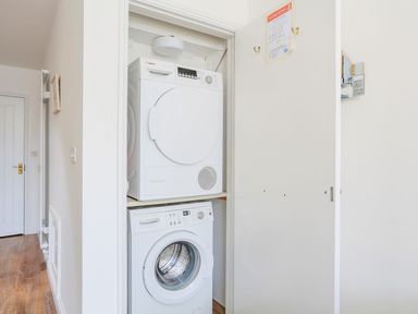 A laundry closet with a stacked washing machine and dryer and a door with fire instructions at 7 Island Quay in Salcombe