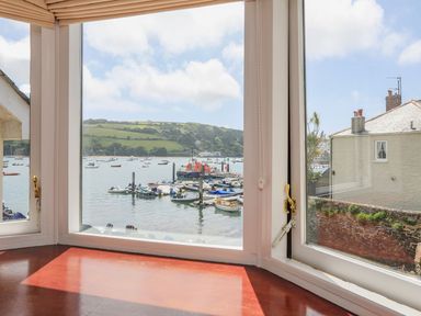 A view of a harbor with boats and a hillside seen through three large glass windows with wooden frames at 7 Island Quay in Salcombe