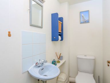 A small bathroom with a white sink and faucet a wall mirror a blue wooden toilet paper holder a white toilet and a small picture of a sailboat on the wall at 7 Island Quay in Salcombe