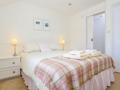 A bedroom with a bed covered with white and plaid linens bedside tables with lamps and folded towels on the bed at 7 Island Quay in Salcombe