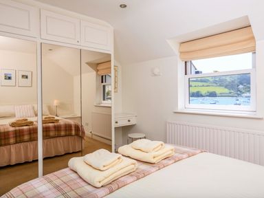 A bedroom with a bed and folded towels near a window overlooking water at 7 Island Quay in Salcombe
