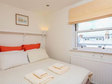A bedroom with a bed with white and red pillows towels on the bed and a window showing rooftops at 7 Island Quay in Salcombe