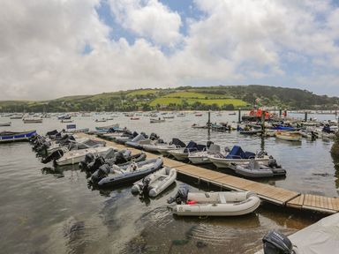 A harbor with multiple small boats docked at wooden piers and hills with houses in the background at 7 Island Quay Salcombe