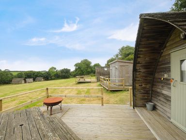 A wooden deck with a fire pit and picnic tables on a grassy area with small wooden cabins at Sheep Shed Penbugle Organic Farm in St Keyne near Looe