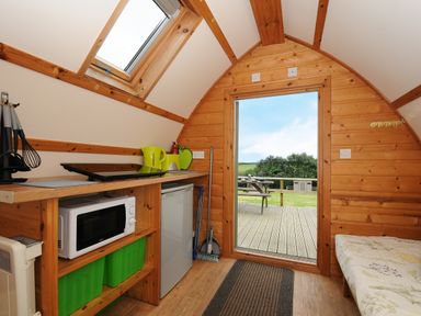 A small wooden cabin interior with a kitchenette microwave fridge door leading to deck and outdoor picnic table Sheep Shed @ Penbugle Organic Farm St Keyne near Looe