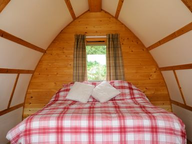A small wooden bedroom with a bed covered in a red and white plaid bedspread and two pillows at Sheep Shed Penbugle Organic Farm St Keyne near Looe