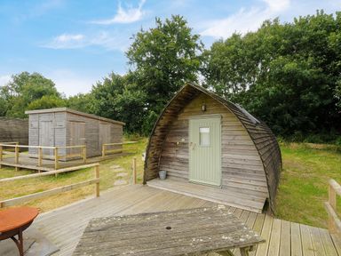 An outdoor area with a curved wooden cabin a rectangular wooden shed a wooden table and railings at Sheep Shed @ Penbugle Organic Farm in St Keyne near Looe