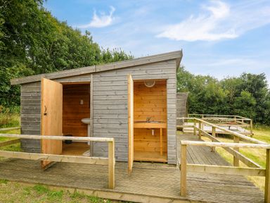 A wooden outdoor structure with two open doors showing a sink and a basin on a wooden deck with railings at Sheep Shed @ Penbugle Organic Farm in St Keyne near Looe