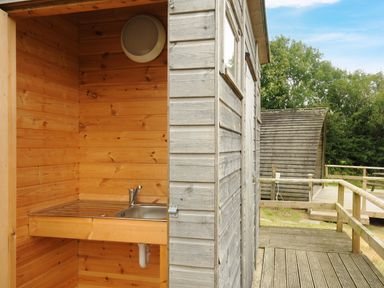 A wooden outdoor sink area attached to a wooden building with a deck and curved wooden structures in the background at Sheep Shed Penbugle Organic Farm St Keyne near Looe