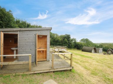 A wooden outdoor washing and bathroom area with small cabins and picnic tables on a grassy field at Sheep Shed @ Penbugle Organic Farm in St Keyne near Looe