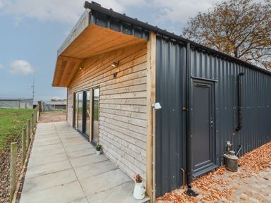 Exterior of a building with wooden and black metal siding a paved walkway and a tree in the background at Elliw in Bontuchel near Ruthin