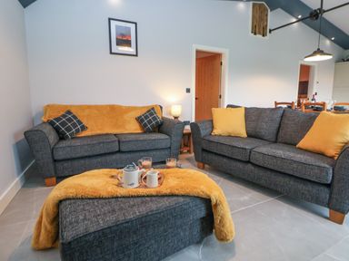 A living room with two grey sofas and a matching ottoman with yellow throw blankets and cushions at Elliw in Bontuchel near Ruthin
