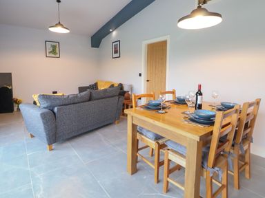 A dining table set with plates glasses and a bottle next to a living area with sofas and a lamp at Elliw in Bontuchel near Ruthin
