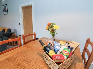 A dining table with a basket containing a bottle of prosecco and assorted food items with flowers in a vase at Elliw in Bontuchel near Ruthin