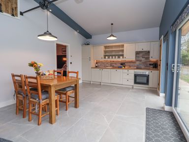 A kitchen with wooden dining table and chairs and white cabinets at Elliw in Bontuchel near Ruthin