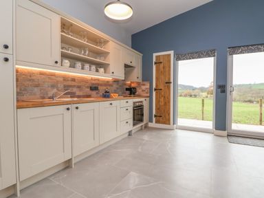 A kitchen with cream cabinets and wood countertop next to two glass doors showing a green field at Elliw in Bontuchel near Ruthin