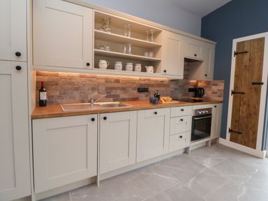 A kitchen with white cabinets wooden countertops a sink stove oven and a wooden door at Elliw in Bontuchel near Ruthin