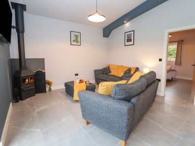 A living room with two grey sofas a wood burning stove and a doorway to a bedroom at Elliw in Bontuchel near Ruthin