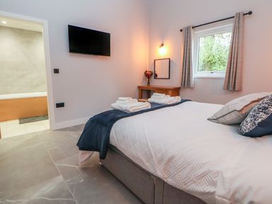 A bedroom with a bed and folded towels a wall-mounted TV a window with curtains and a vanity table with flowers at Elliw in Bontuchel near Ruthin