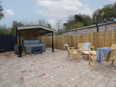 An outdoor patio area with a covered hot tub and wooden chairs and tables with towels on them at Elliw in Bontuchel near Ruthin