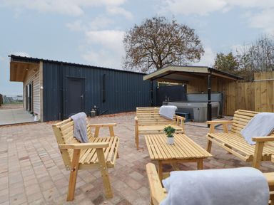 An outdoor patio area with wooden chairs and a table with a plant and a covered hot tub at Elliw in Bontuchel near Ruthin