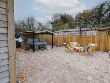 An outdoor patio with a covered hot tub and wooden seating area with table and chairs at Elliw in Bontuchel near Ruthin