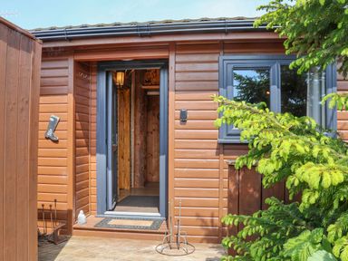 An open doorway of a wooden cabin with a doormat and green plants outside at Stag Lodge Holiday Retreat in Whitby