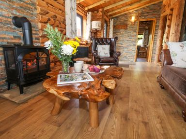 A living room with a wooden coffee table with flowers cups and muffins a leather armchair and a wood burning stove at Stag Lodge Holiday Retreat Whitby
