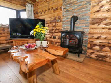 A wooden log cabin living room with a rustic coffee table flowers on the table a television and a black wood stove at Stag Lodge Holiday Retreat Whitby