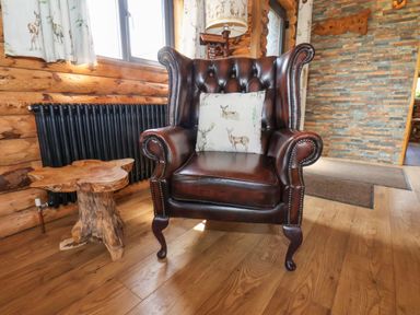 A brown leather armchair with a cushion next to a wooden stump side table in a room with wooden walls and floor at Stag Lodge Holiday Retreat Whitby