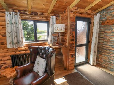 A wooden room with a leather armchair a window curtains a door and a lamp at Stag Lodge Holiday Retreat Whitby