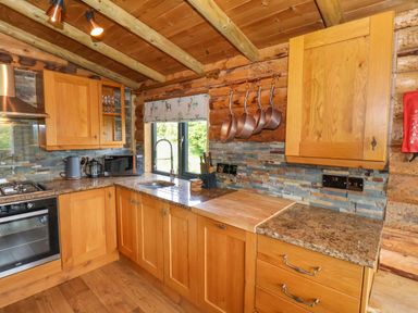 A kitchen with wooden cabinets hanging copper pots a window above the sink and countertop appliances at Stag Lodge Holiday Retreat Whitby